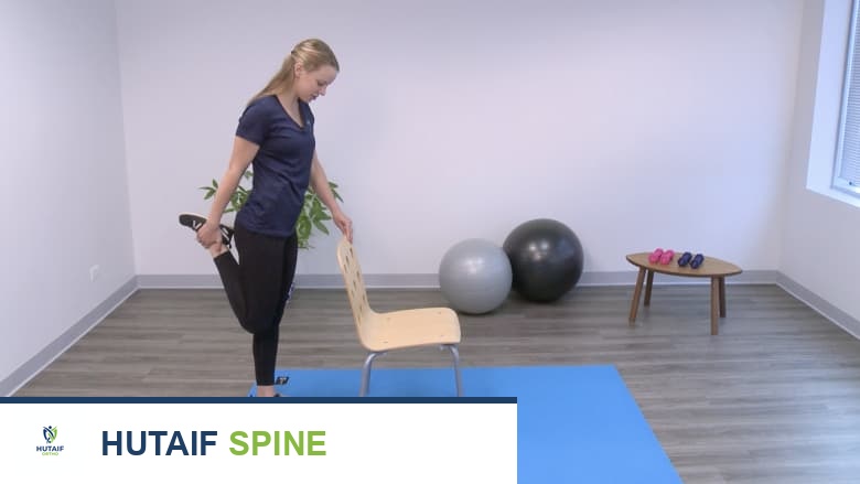 امرأة تؤدي تمرين إطالة العضلة الرباعية في وضعية الوقوف، ممسكة بساقها اليمنى.